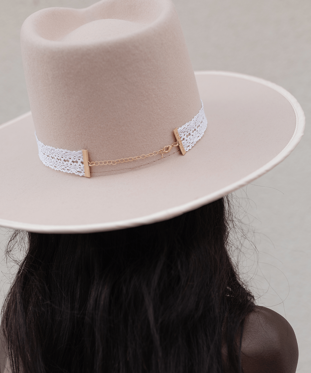 Woman wearing a cream hat with a white lace band facing behind against a plain background #color_white