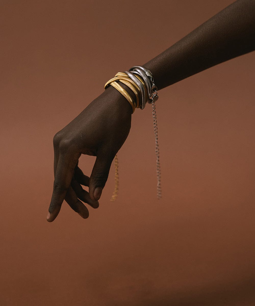 Close up image of someone's hand with a gold and silver chain band around the wrist against a brown background 