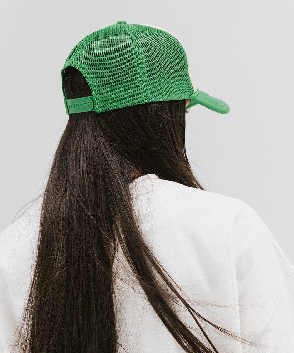 Woman with long hair wearing a cream and vintage green cap and a white t-shirt against a plain background  #color_cream - vintage green