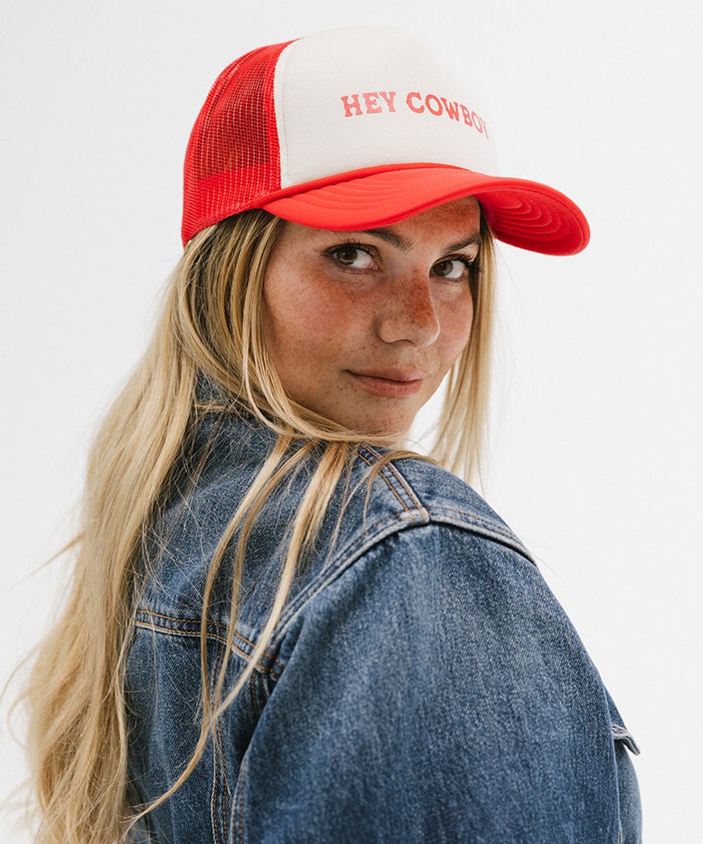 Woman wearing a cream and vintage red cap with 'Hey Cowboy' text and a denim shirt, posing sideways against a plain background  #color_cream - vintage red