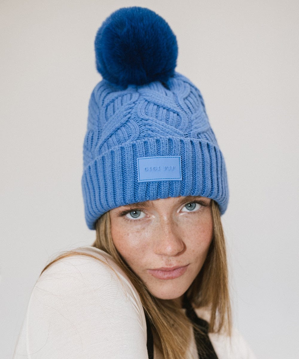 Woman wearing an arctic blue colored knit beanie with a pom-pom and a white t-shirt against a plain background #color_arctic blue