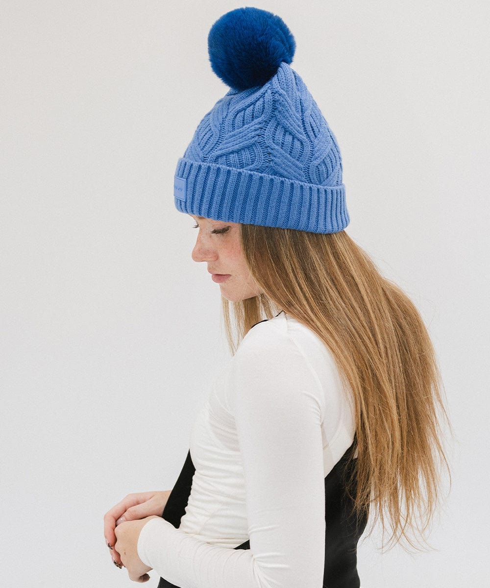Woman wearing an arctic blue colored knit beanie with a pom-pom and a white t-shirt, facing sideways against a plain background #color_arctic blue