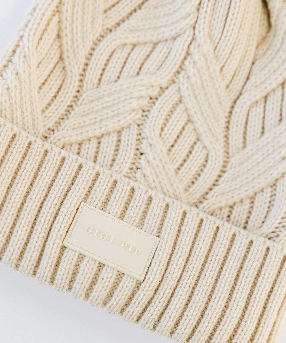 Close up image of a cream knit beanie with with the brand label on a plain background #color_cream