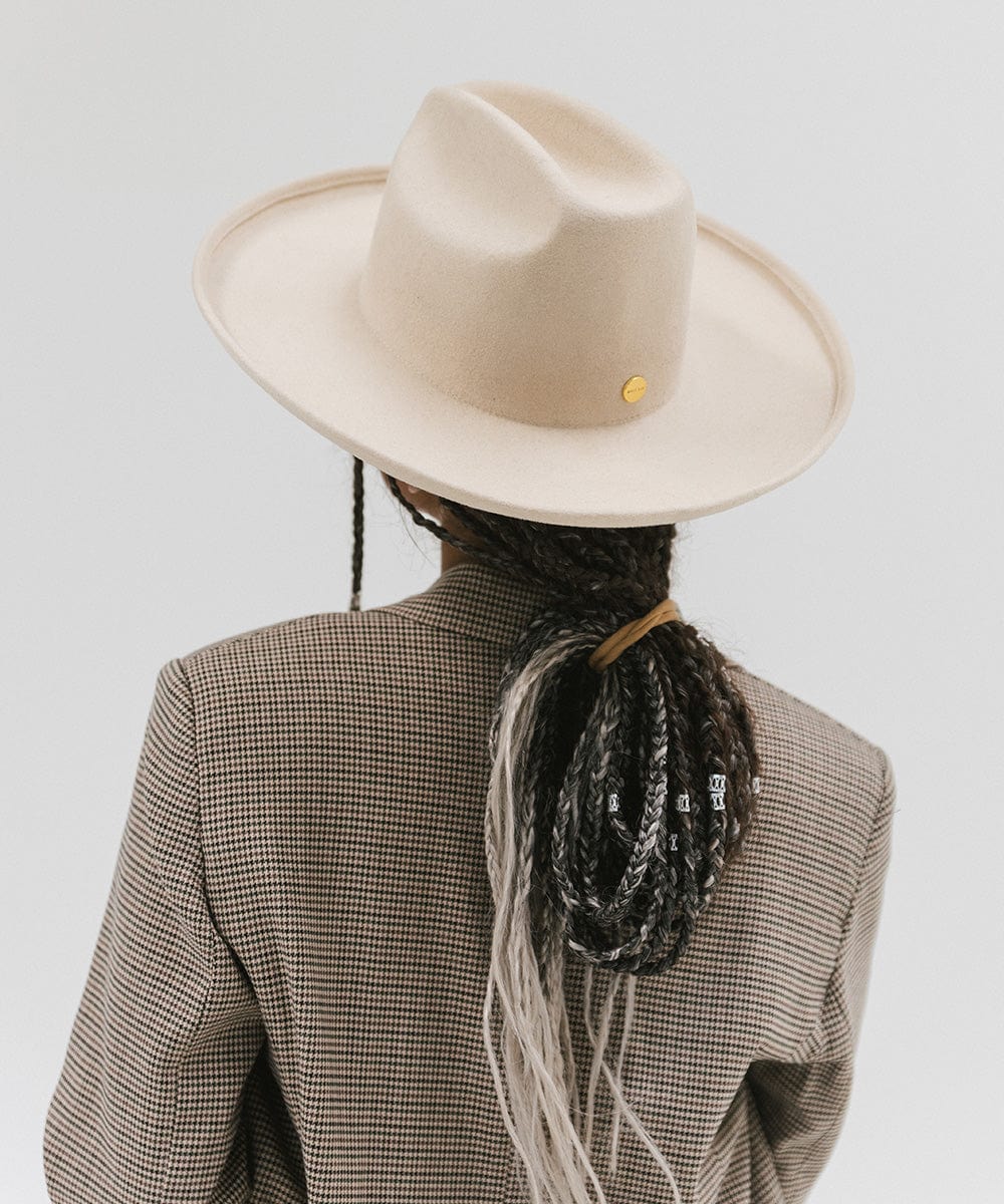 Person wearing an off white western hat with a pencil brim and a tall crown and coat against a plain background #color_off white