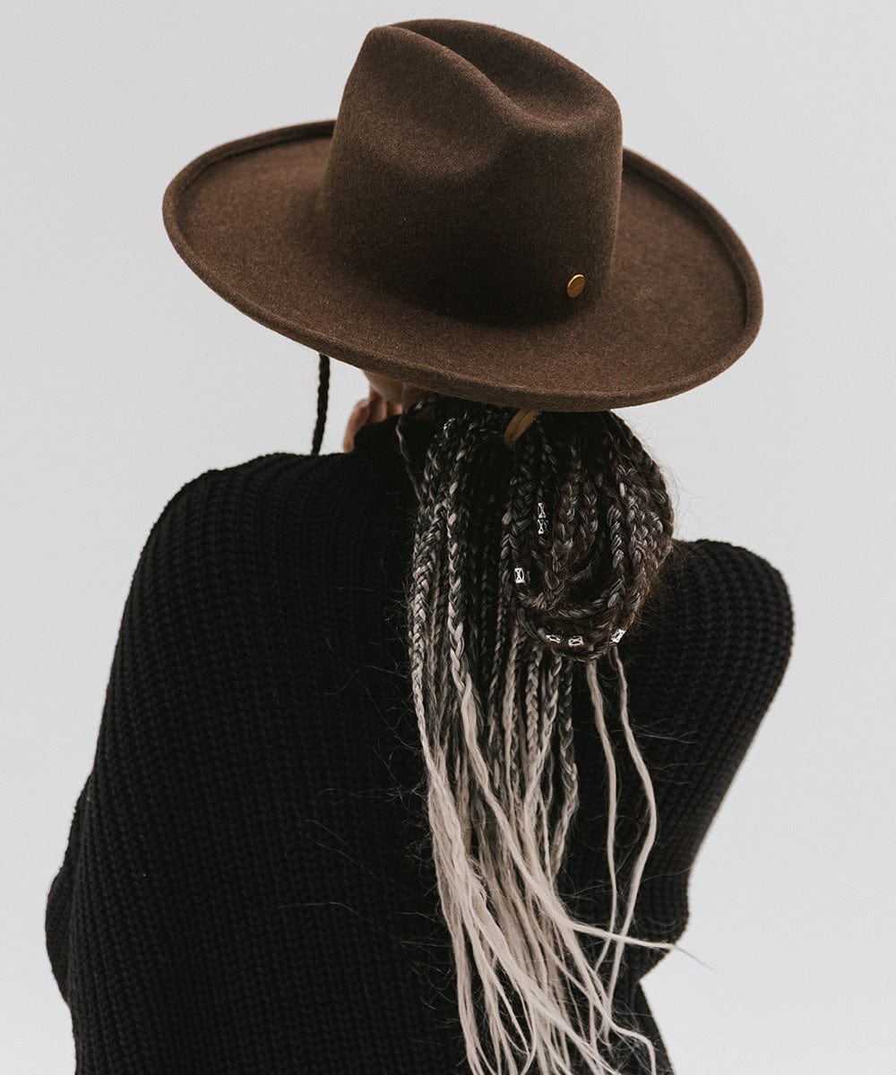 Person wearing a mix brown colored western hat with a pencil brim and a tall crown, and a black sweater against a plain background  #color_mix brown