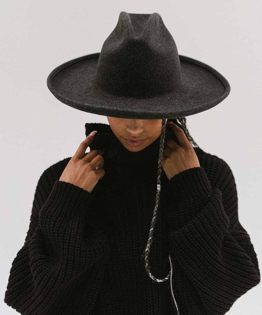 Person wearing a mix charcoal colored western hat with a pencil brim and a tall crown and a black sweater against a plain background  #color_mix charcoal