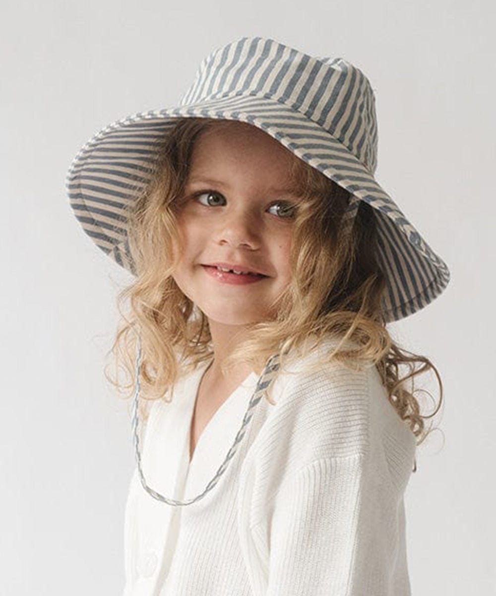 Young girl wearing a blue and white striped bucket hat and a white shirt against a plain background #color_striped - blue