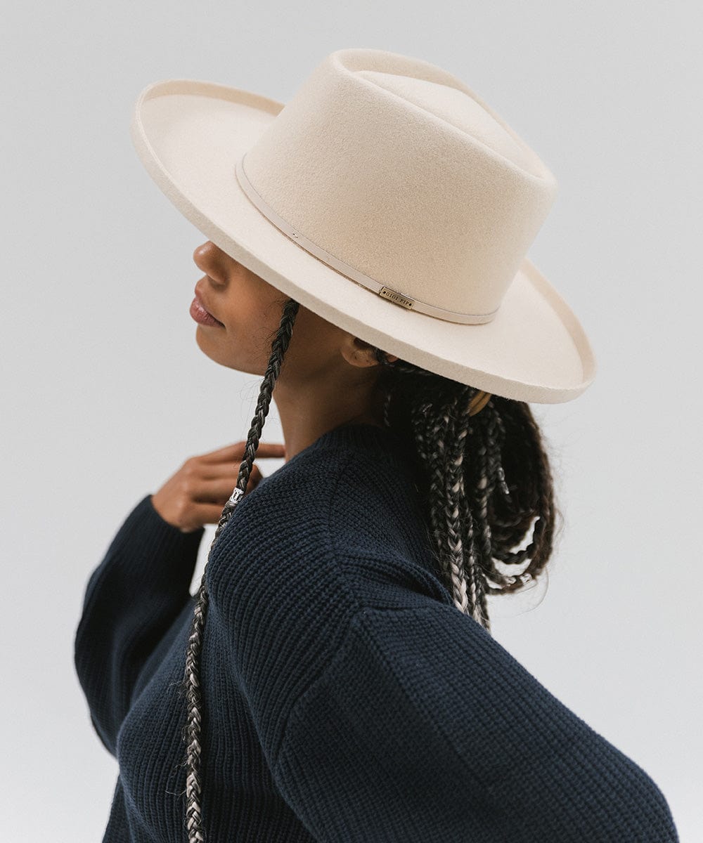 Woman wearing a cream Lennon pencil brim fedora hat with a hat band and a blue sweater, facing sideways against a plain background #color_cream