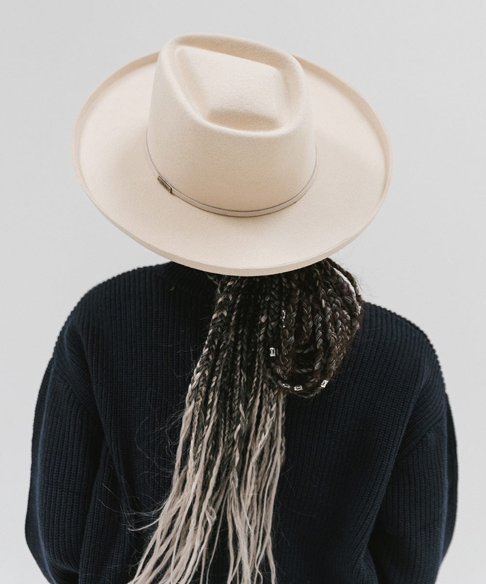 Person wearing a cream Lennon pencil brim fedora hat with a hat band and a blue sweater against a plain background #color_cream