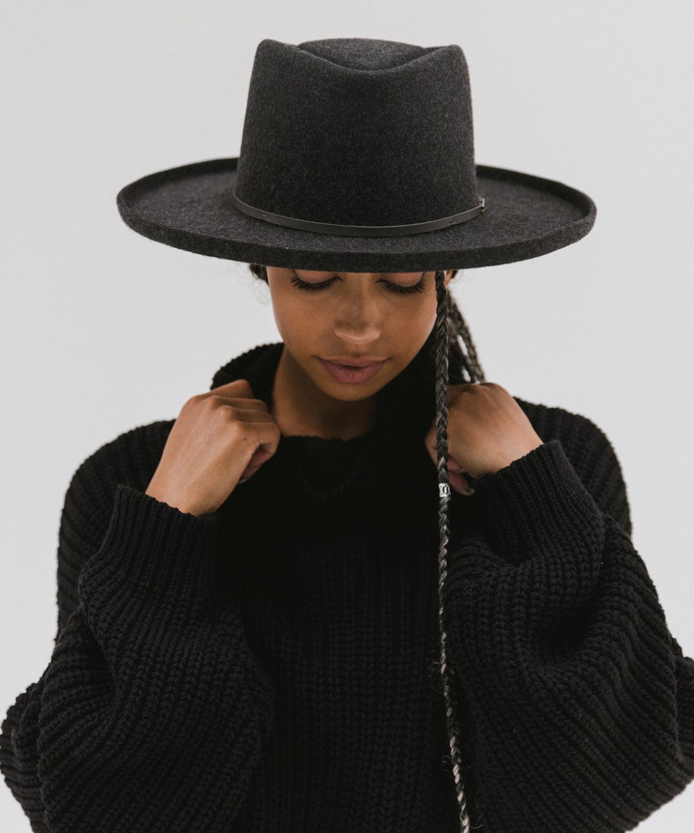 Woman wearing a mix charcoal colored Lennon pencil brim fedora hat with a hat band and a black sweater against a plain background #color_mix charcoal