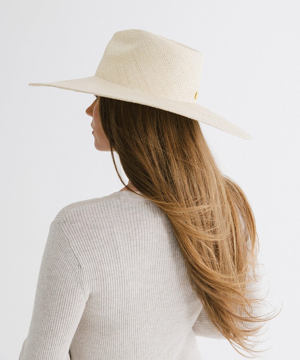 Woman with long hair wearing a natural colored wide brim straw hat and a white top, facing behind against a plain background  #color_natural
