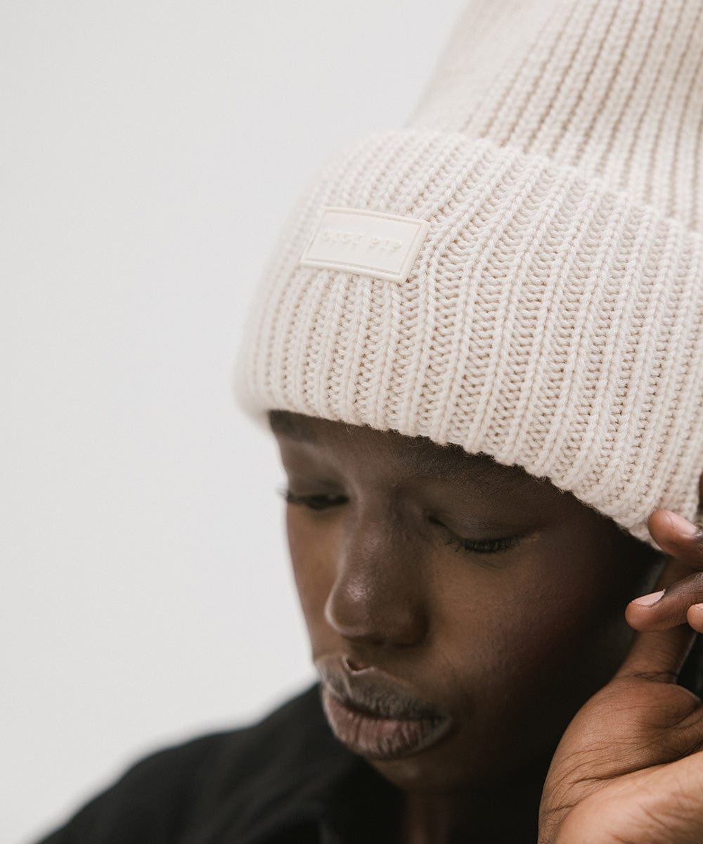 A person wearing an off white  colored ribbed beanie against a plain background #color_off white