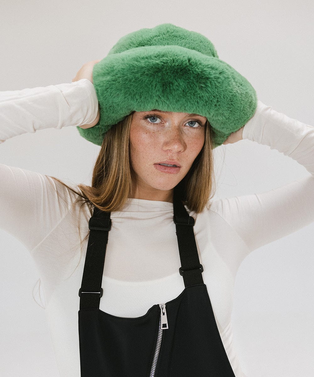 Woman wearing a green faux fur bucket hat and a white top with a black zipper against a plain background #color_evergreen