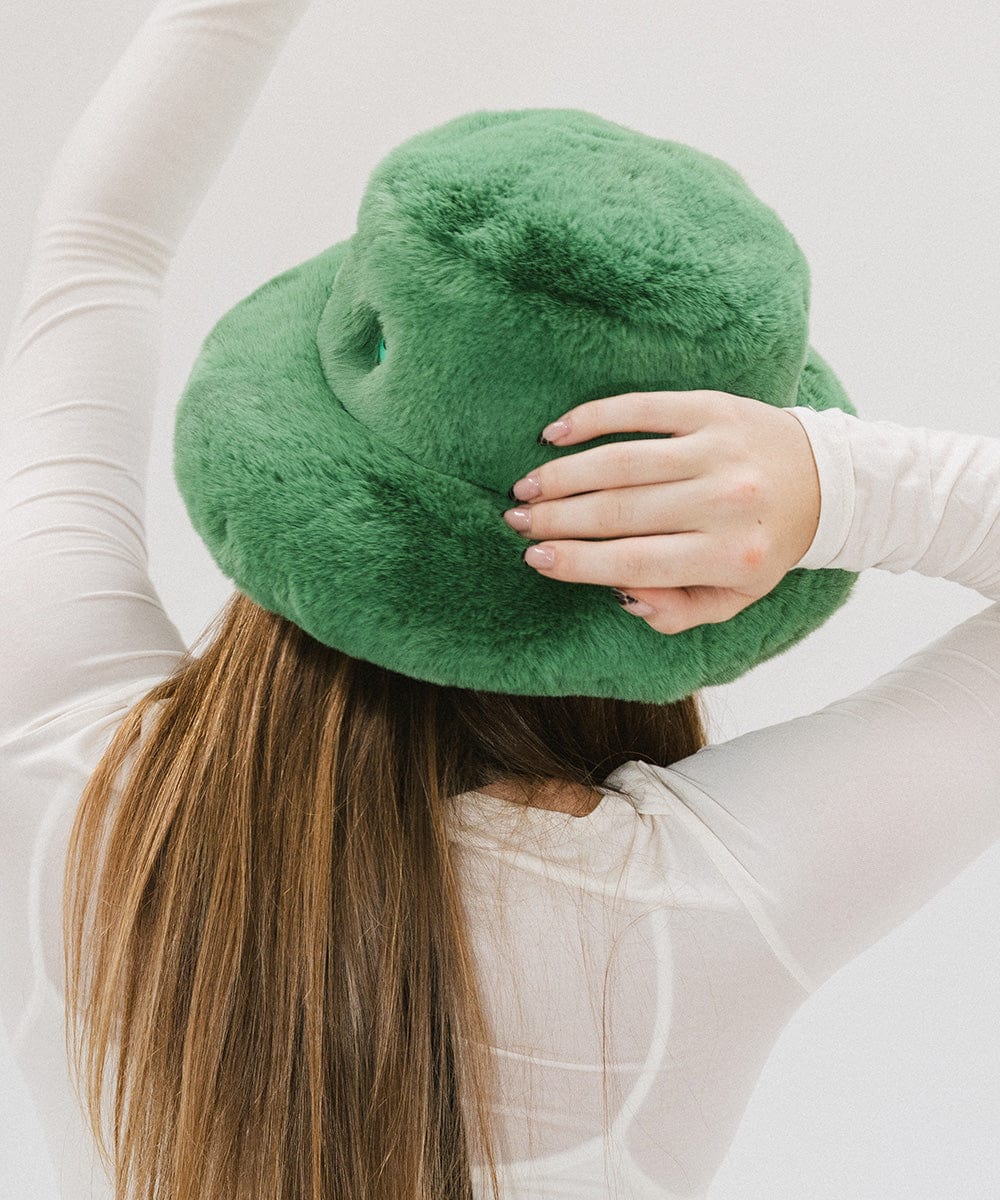 Person with long hair wearing a green faux fur bucket hat and a white top against a plain background #color_evergreen