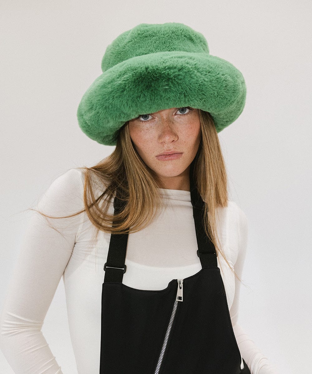 Woman wearing a green faux fur bucket hat and a white top with a black zipper against a plain background #color_evergreen
