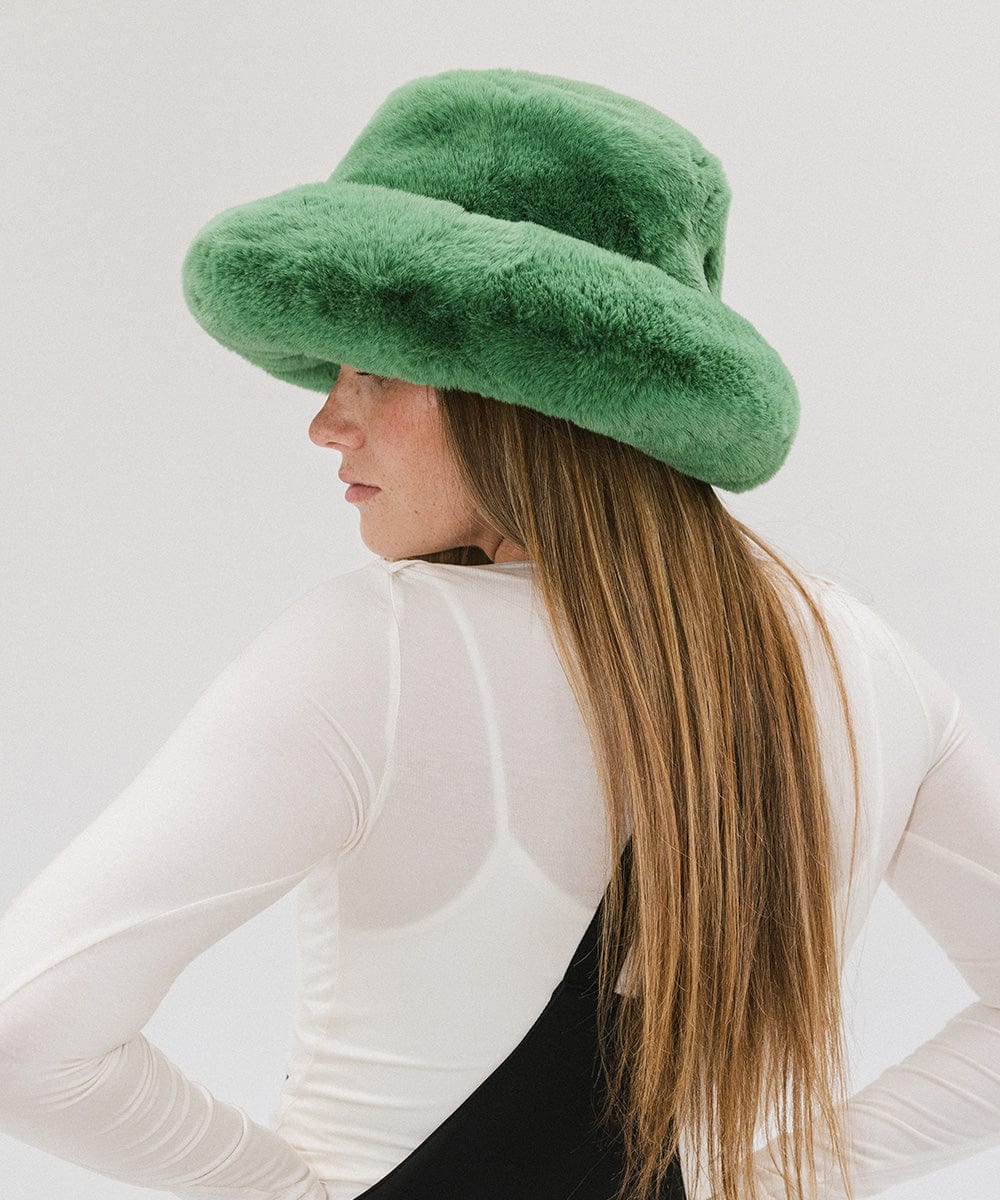 Woman with long hair wearing a green faux fur bucket hat and a white top against a plain background #color_evergreen