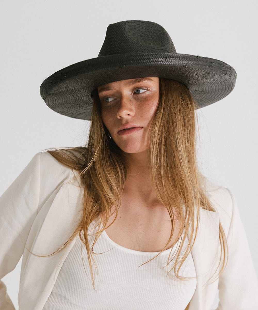 Woman wearing a black pencil brim straw hat and a white top with a white blazer against a plain background #color_black