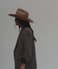 Woman wearing a brown cowboy hat and a blazer, posing against a plain background #color_brown