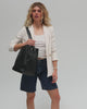 Woman wearing a white top with a white blazer and denim shorts, carrying a black Dia everyday leather tote bag, posing against a plain background #color_black