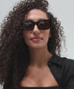 Woman wearing tortoise pattern sunglasses and a black shirt, posing against a plain background  #color_tortoise