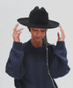 Woman wearing a black Western hat with a classic cattleman crown and a black hat band, and a dark blue sweatshirt, posing against a plain background  #color_black