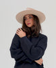 Woman wearing a cream Emery Teardrop Fedora Hat with a hat band  and a dark blue sweatshirt, posing against a plain background #color_cream