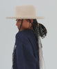 Woman wearing a cream Lennon pencil brim fedora hat with a hat band and a blue sweater, posing against a plain background #color_cream