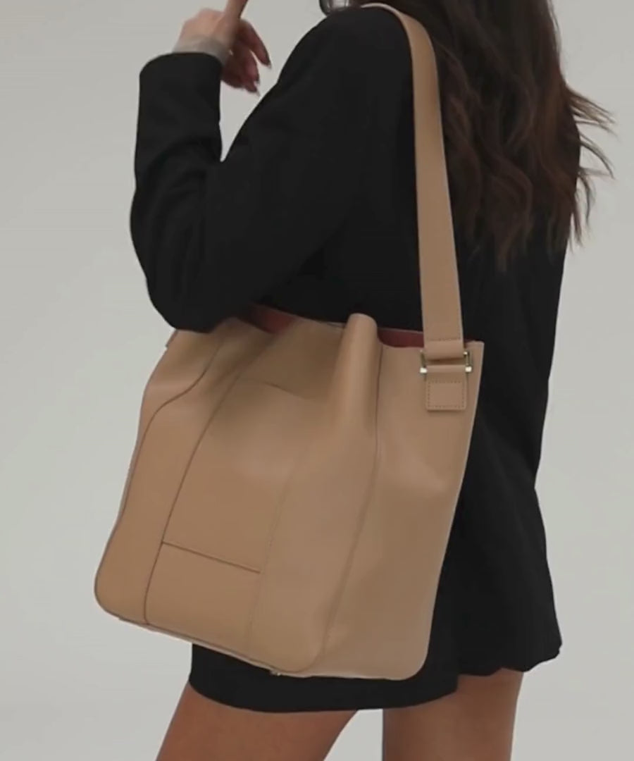 Person wearing a black outfit carrying a tan Dia everyday leather tote bag, posing against a plain background #color_tan