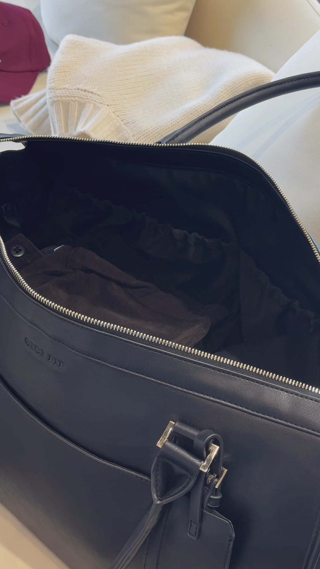 Person keeping clothes and valuables inside a black vegan leather weekender bag on a sofa #color_black