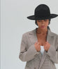 Woman wearing a black fedora hat with a hat band and a white top with a checkered coat posing against a plain background #color_black