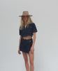 Woman with long blonde hair wearing a tan fedora hat, a denim top and a denim skirt, posing against a plain background  #color_tan