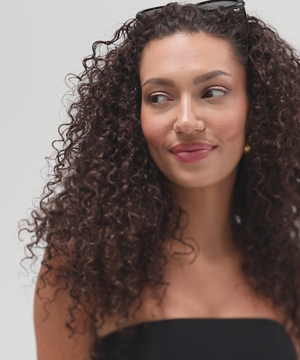 Woman with curly hair wearing black sunglasses and a black top, posing against a plain background #color_black