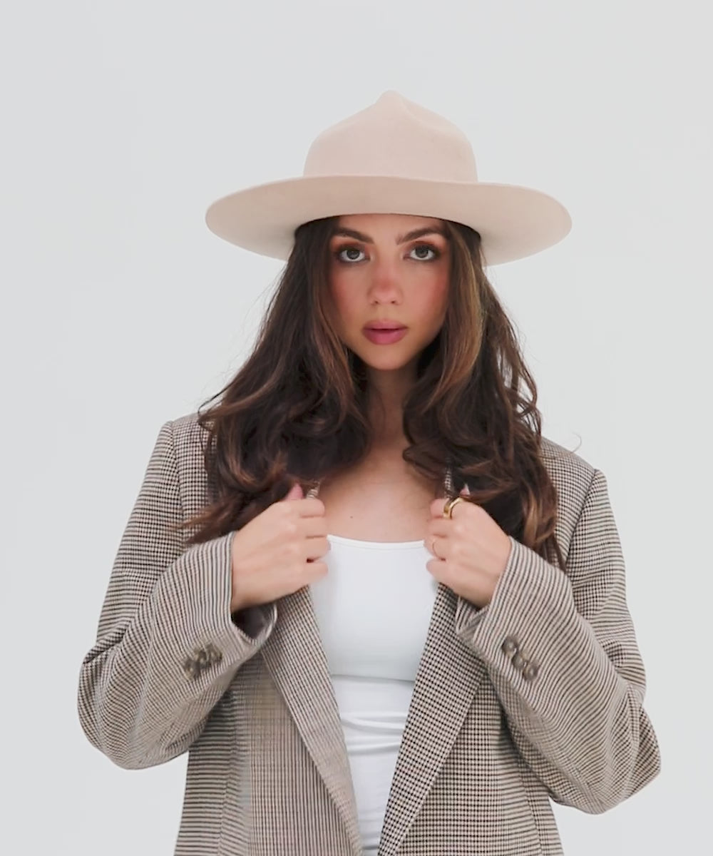 Woman wearing a cream fedora hat with a hat band and a white top with a checkered coat posing against a plain background #color_cream