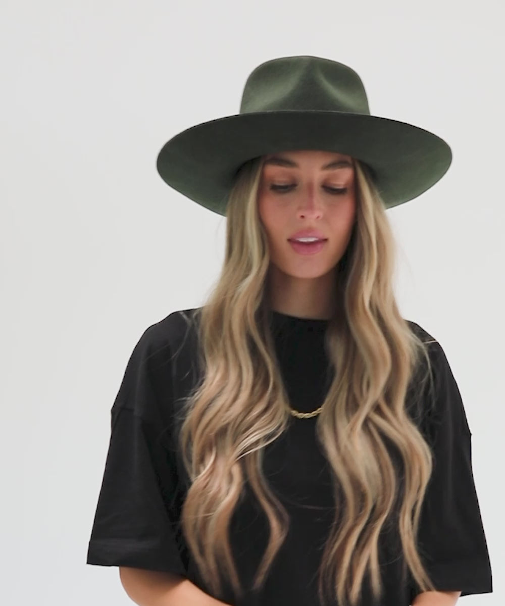 Woman wearing a dark green fedora hat and a black t-shirt against a plain background #color_dark green