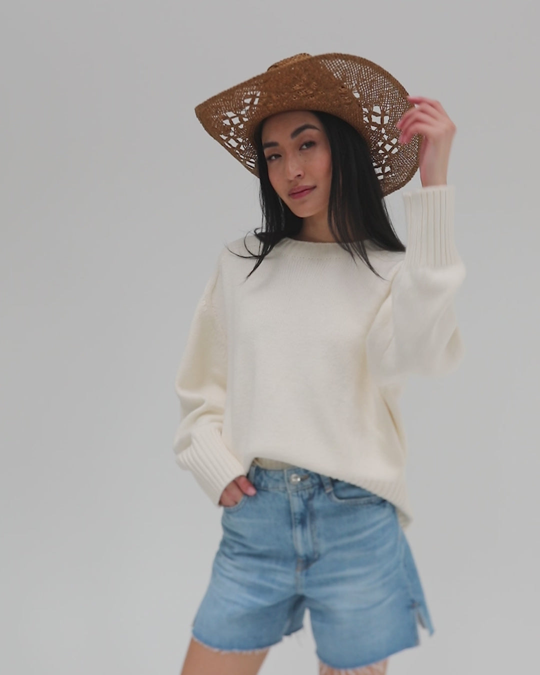 Woman wearing a honey colored paper rope straw cowboy hat, a white sweatshirt and blue shorts, posing against a plain background #color_honey