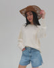 Woman wearing a honey colored paper rope straw cowboy hat, a white sweatshirt and blue shorts, posing against a plain background #color_honey