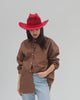 Woman wearing a cherry red colored paper rope straw cowboy hat, a brown shirt and blue jeans, posing against a plain background #color_cherry red