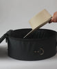 Hats being packed in a round black hat travel case and being carried by a woman wearing a grey outfit #color_black