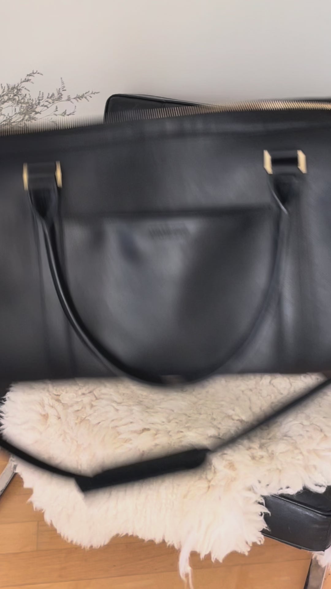 Person storing a number of different things inside a black vegan leather weekender bag on a chair #color_black