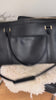 Person storing a number of different things inside a black vegan leather weekender bag on a chair #color_black