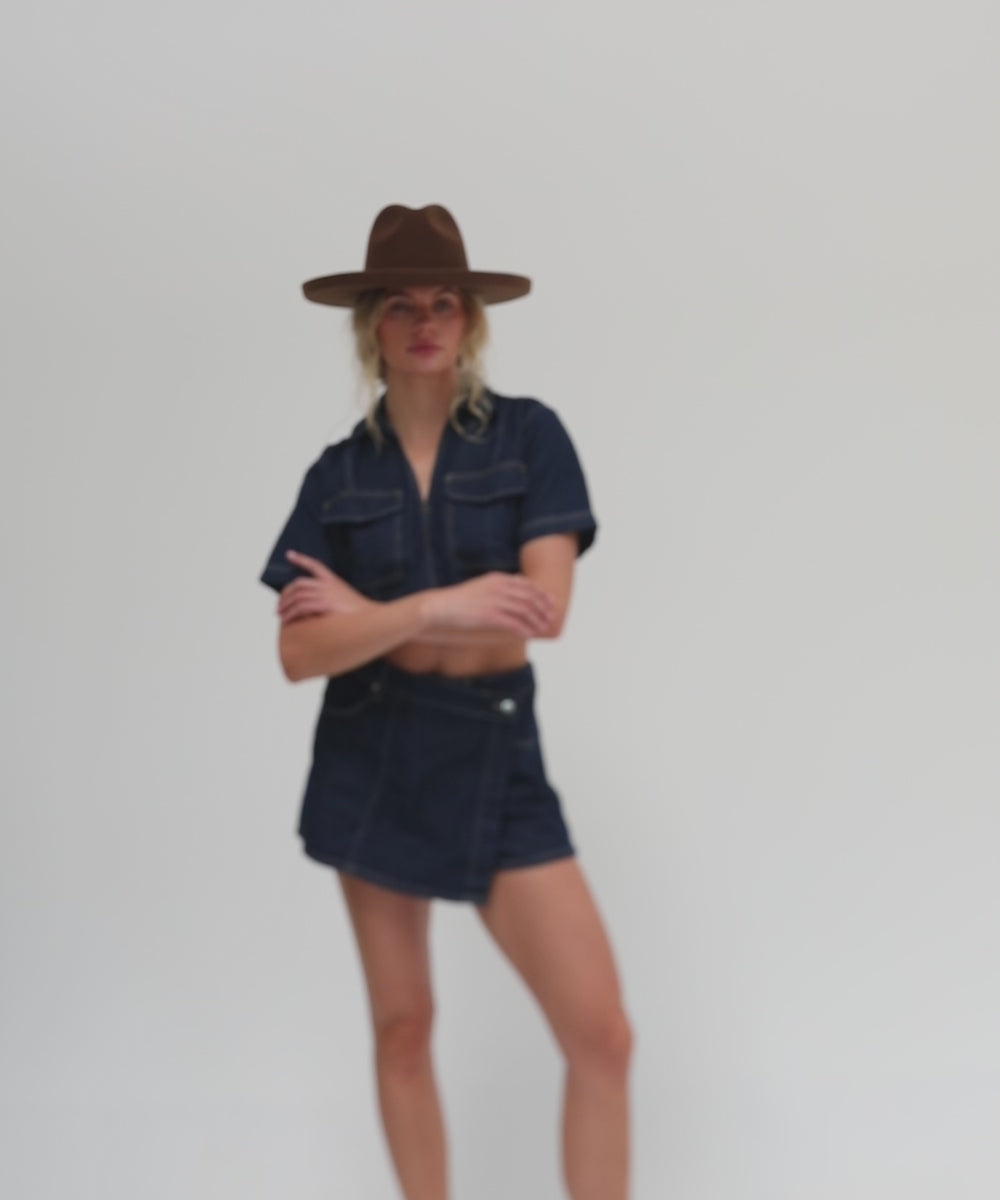 Woman wearing a chocolate colored pencil brim felt fedora hat, a denim shirt and denim skirt, posing against a plain background #color_chocolate