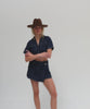 Woman wearing a chocolate colored pencil brim felt fedora hat, a denim shirt and denim skirt, posing against a plain background #color_chocolate