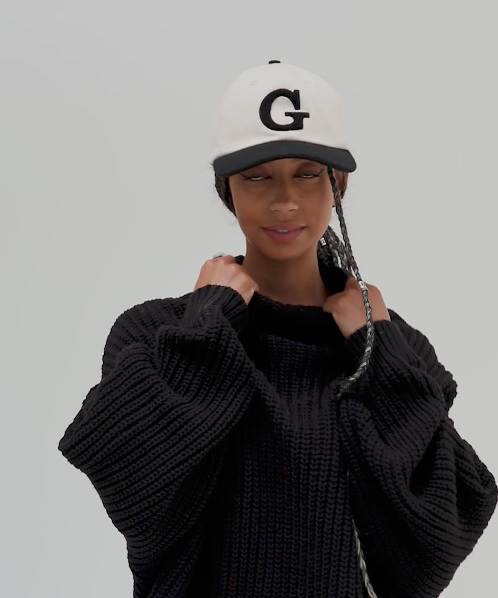 Woman wearing a cream and black baseball cap with the letter 'G' and a black sweater, posing against a plain background  #color_cream-black