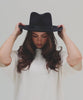 Woman wearing a navy fedora hat with a band and a white t-shirt, posing against a plain background #color_navy