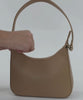 Person inserting various items into a tan genuine leather handbag on a plain background #color_tan