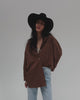Woman wearing a black cowboy hat, a brown shirt and light blue jeans, posing against a plain background #color_black