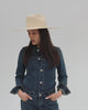 Woman wearing a natural colored western wide brim straw hat, a denim jacket and jeans against a plain background #color_natural