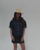 Woman wearing a natural colored wide brim fedora straw hat, a denim shirt and a denim skirt against a plain background #color_natural