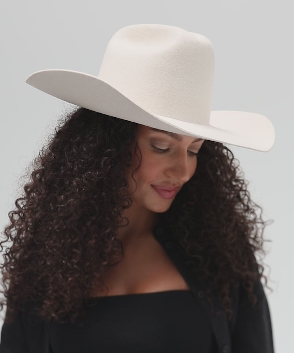 Woman wearing an off white cowboy hat and a black top with a black shirt, posing against a plain background
#color_off white