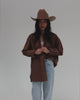 Woman wearing a brown cowboy hat, a brown shirt and light blue jeans, posing against a plain background #color_brown